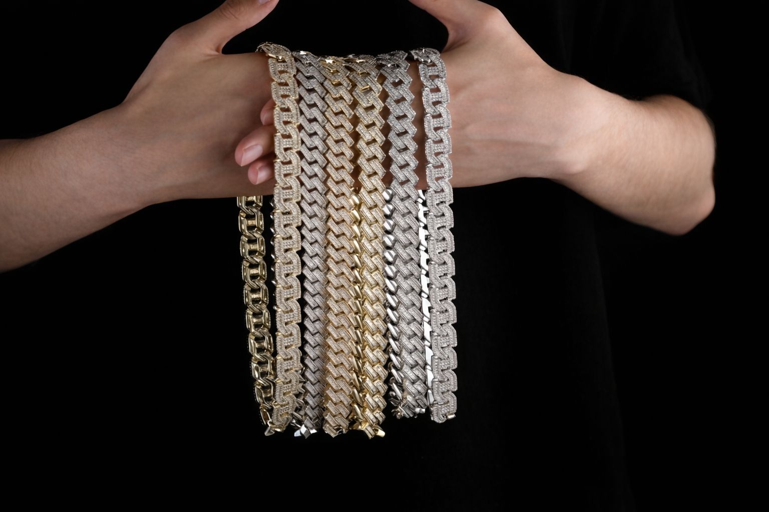 Två händer håller upp ett urval av glänsande Bismarckhalsband i guld och silver.