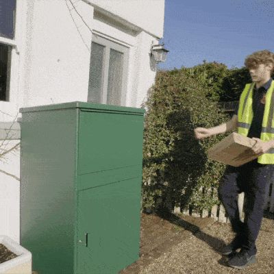 Bud med paket går mot grön paketbox vid hus, under blå himmel.